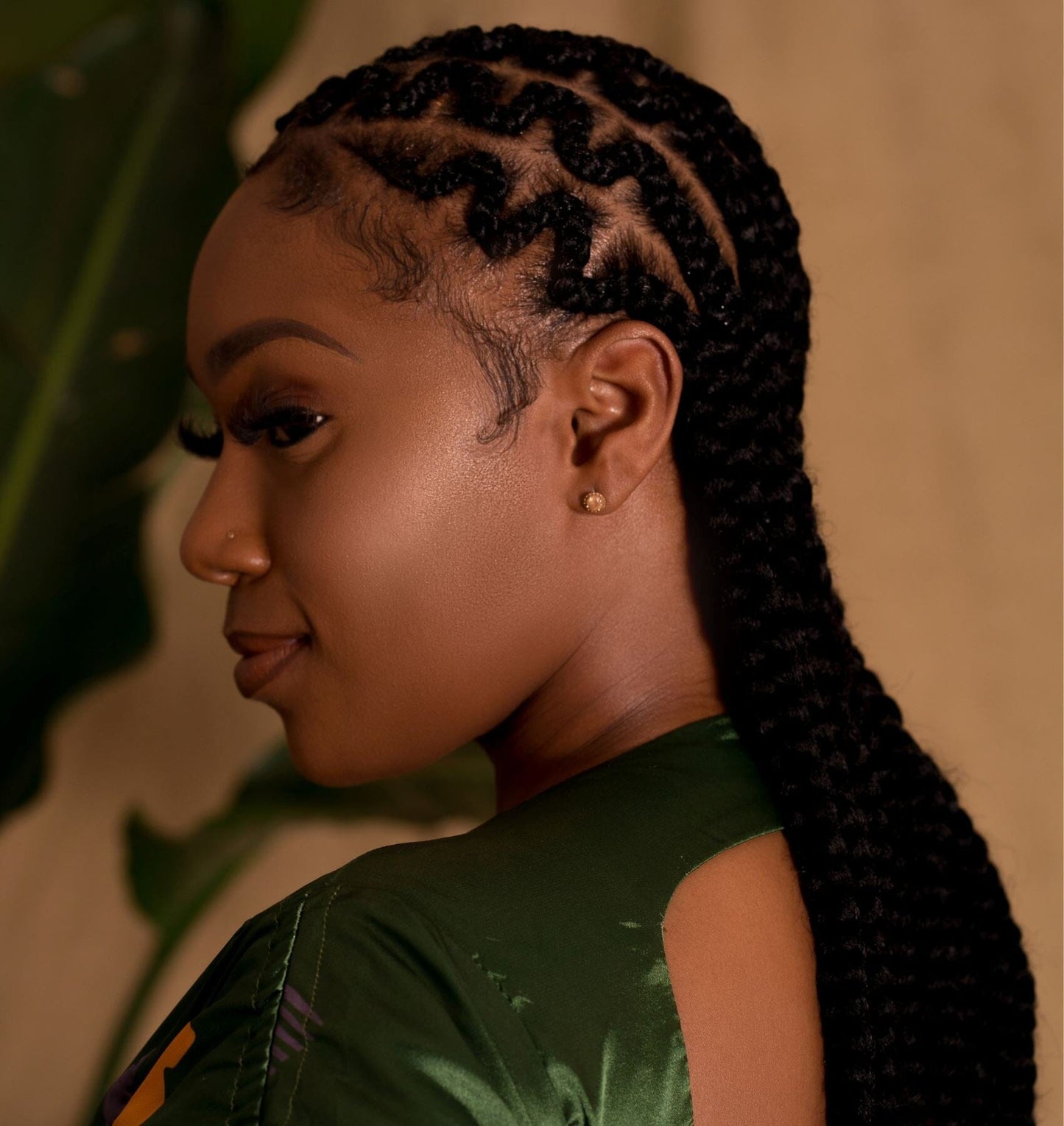 Close-up of a woman's profile in a green satin dress. She has long black hair braided in cornrows.