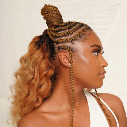 Side profile of a woman with a half-updo with the top of her hair braided and wrapped into a topknot, and the back loose in waves.