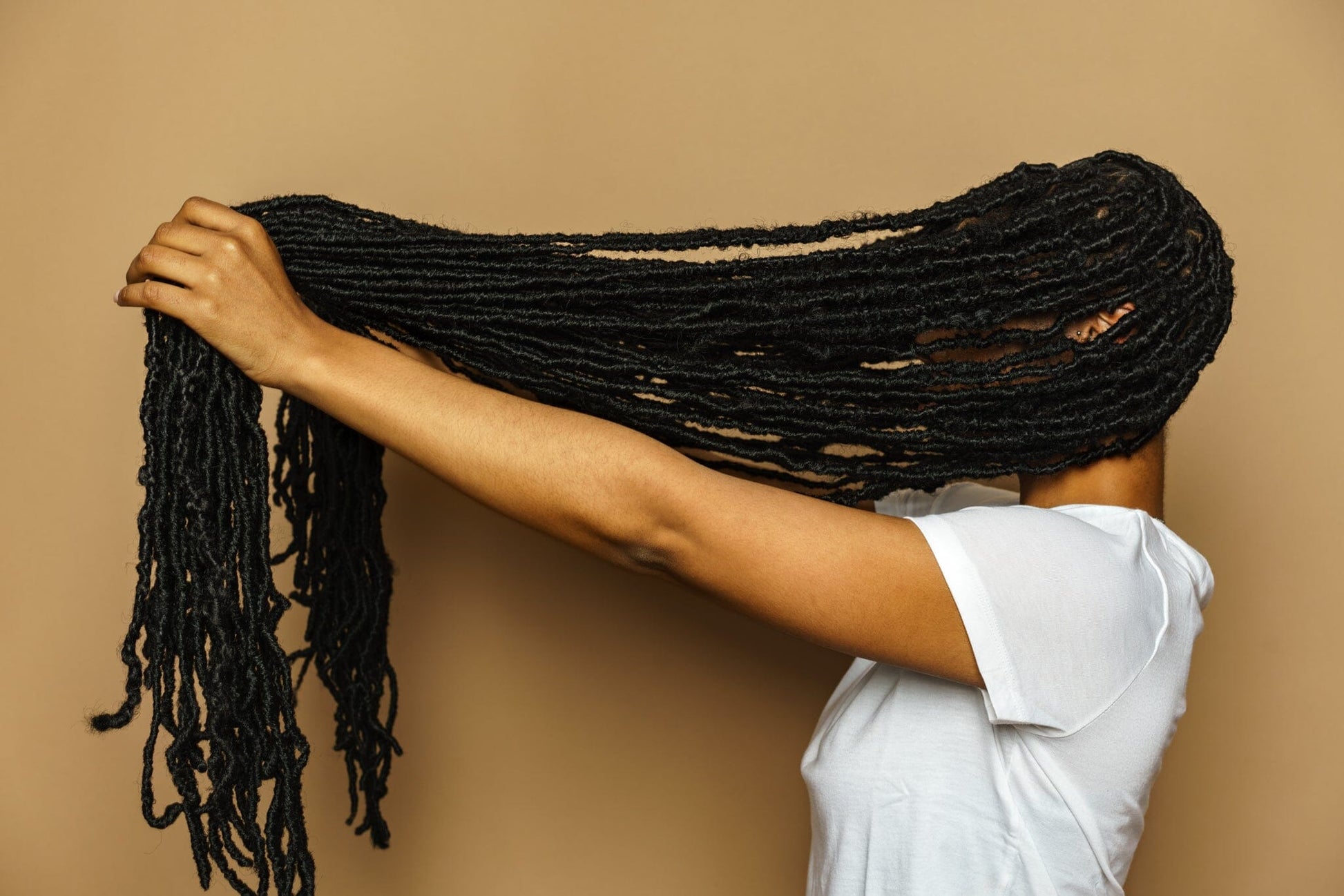 Side profile of a black woman holding her long black locs in front of herself, covering her face. 